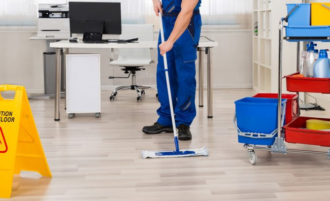 mopping office wood floor with flat mop and putting caution wet floor sign