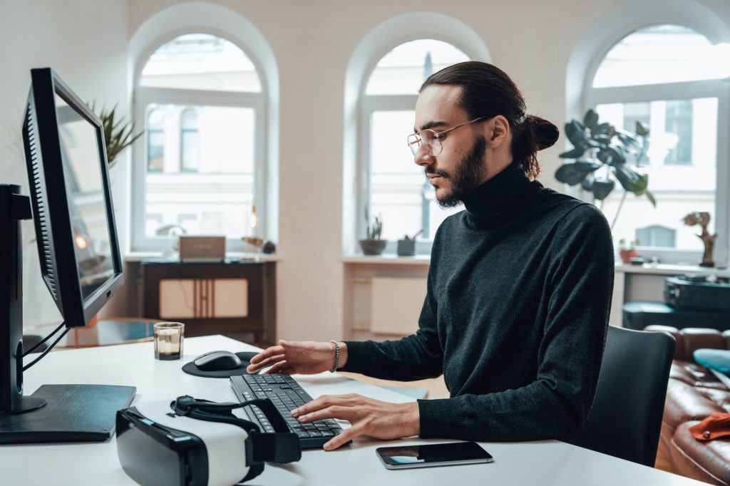 Bearded office worker with long hairs types on keyboard in office