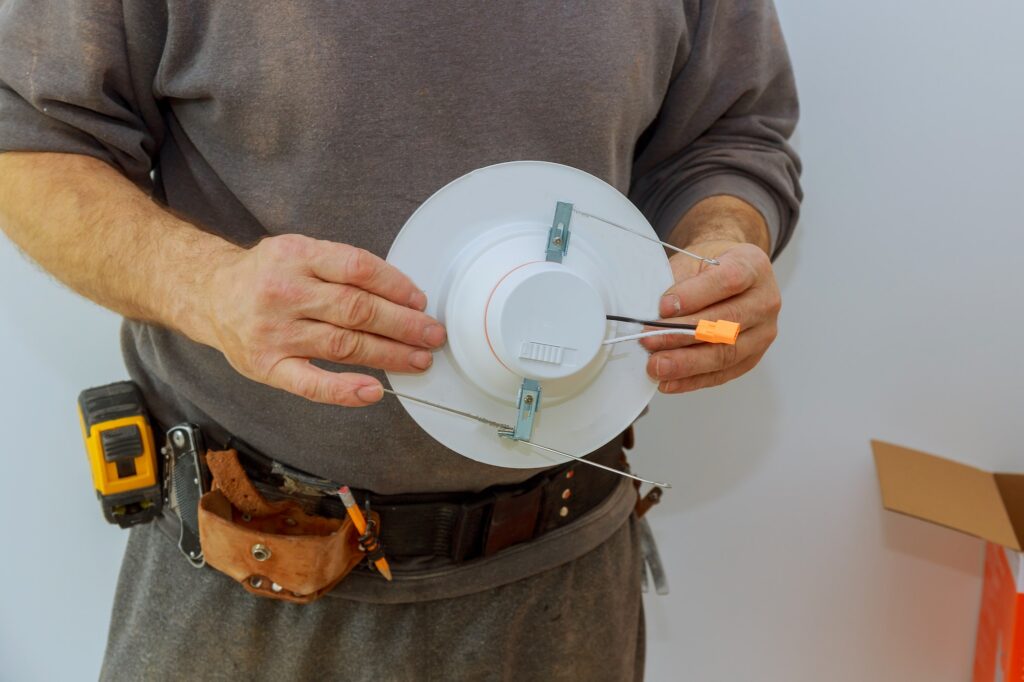 Man is installing electrical light in the ceiling maintenance replacing repair works in the flat.